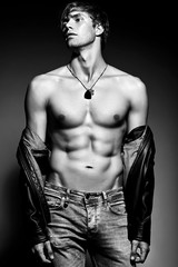 Young handsome muscled fit male model man posing in studio showing his abdominal muscles in  leather jacket