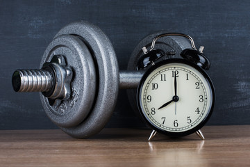 Obraz na płótnie Canvas barbell on a gray background and retro alarm clock. Time 8:00