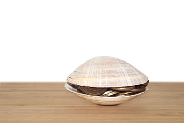 A sea shell with coins inside on wooden table white background