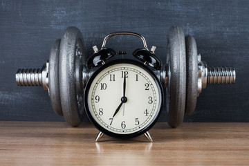 Obraz na płótnie Canvas barbell on a gray background and retro alarm clock. Time 7:00