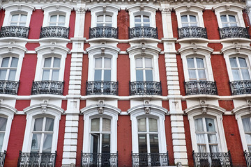 Red painted brick facade with white decorations around arched windows and balconies of a british apartment building in London City