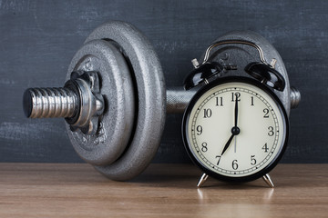 Obraz na płótnie Canvas barbell on a gray background and retro alarm clock. Time 7:00