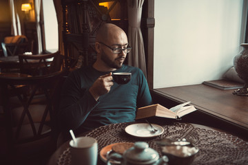 a young man with glasses sitting in a cafe and reading a book