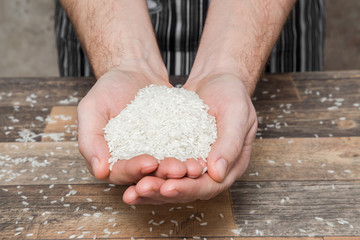 Rice in the hands on the wooden table in the kitchen. Healthy eating and lifestyle.