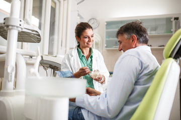 Female dentist in dental office talking with senior male  patient and preparing for treatment.
