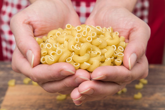 Pasta Macaroni In The Hands On The Wooden Table In The Kitchen. Healthy Eating And Lifestyle.