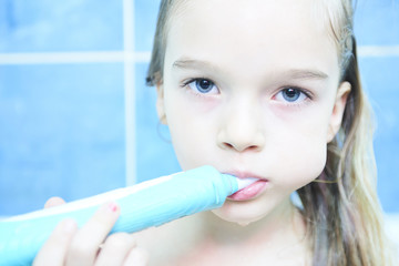 Close up of cute little girl in a bath and cleaning her teeth with electrical toothbrush against...