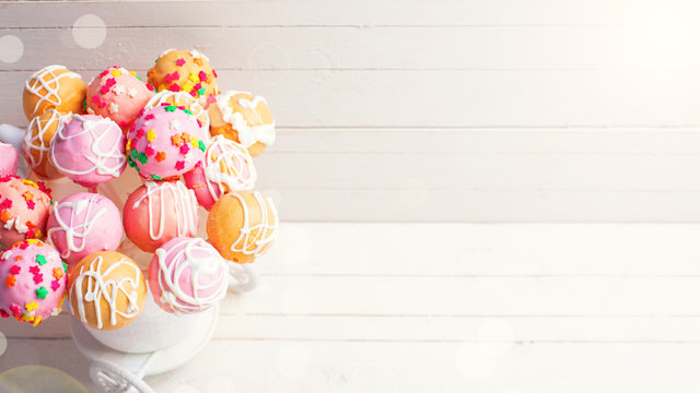 Bright cake pops in ray of light   on white wooden background.