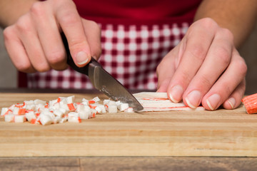 Hands cutting crab sticks on the wooden board in the kitchen. Healthy eating and lifestyle.