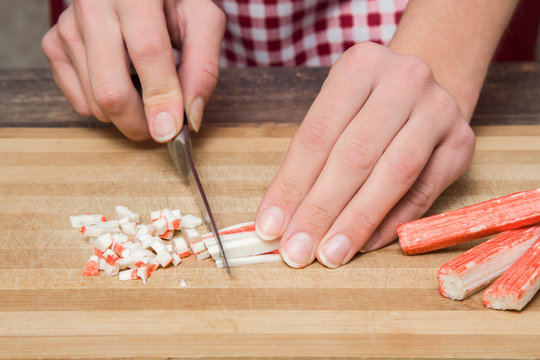 Hands cutting crab sticks on the wooden board in the kitchen. Healthy eating and lifestyle.