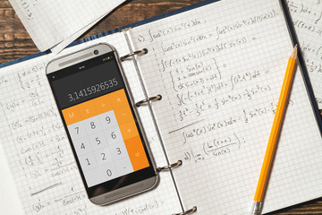 Solving mathematical problems in a notebook .  Phone with calculator app on wooden desk.