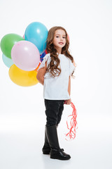 Beautiful little girl standing and holding colorful balloons behind her