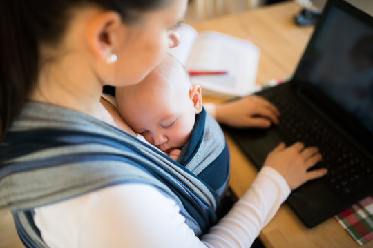 Unrecognizable mother with son in sling, writing on notebook