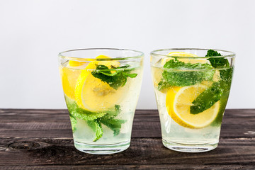 Two clear glasses of Fresh sweet cold carbonated homemade lemonade with lemon slices and mint leaves on old dark grey rustic wooden table.