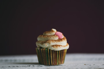 Cupcake decorated with cream, chocolate and heart shape candies on wooden table.