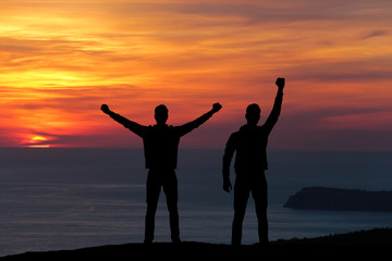 Fototapeta premium silhouette of two men standing on a rock looking into the distance