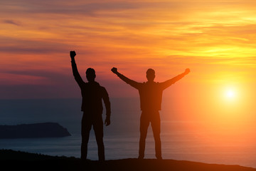 silhouette of two men standing on a rock looking into the distance