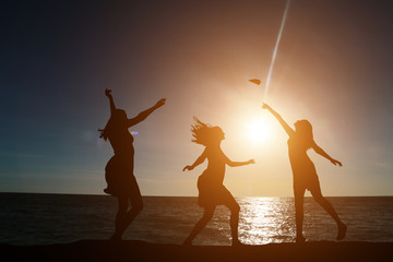Three girls dancing in silhouette against the background of a beautiful sunset and sea