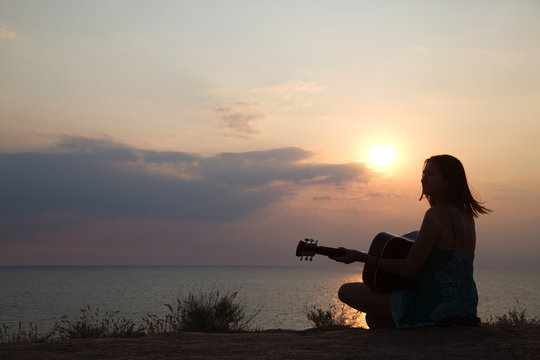 silhouette of girl playing the guitar on the background of the sea and a beautiful sunset