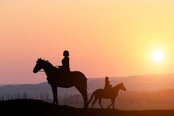 silhouette two girls ride on a horse on a background of a beautiful sunset