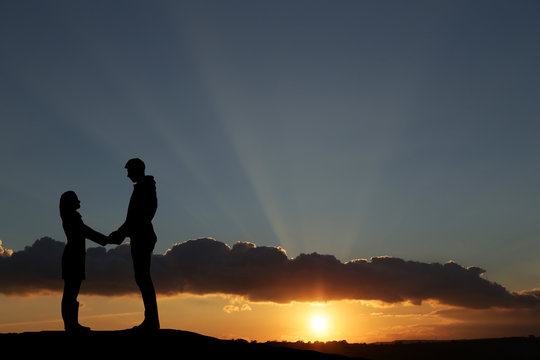silhouette guy and girl on a beautiful sunset holding hands