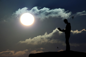 silhouette of a man atop a mountain working on a laptop on the background of beautiful species