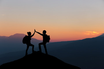 Male and female hikers climbing up mountain cliff and one of them giving helping hand. People helping and, team work concept.