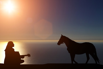 silhouette of a horse walks by the sea and a girl playing a guitar on a background of a beautiful sunset