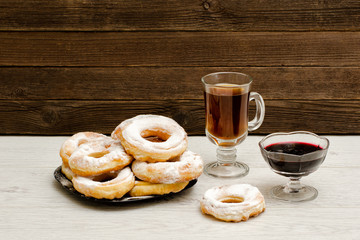 Donuts in powdered sugar, a mug of tea and currant jam on a wooden background