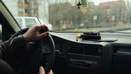Adult man in leather jacket driving old car through town and smoking cigarette, the look and feel of 1990s.