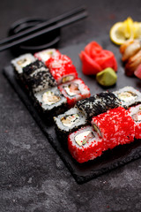 Japanese cuisine. Sushi set on a stone plate and black concrete background.