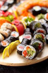 Japanese cuisine. Sushi set on a round wooden board over black concrete background.