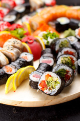 Japanese cuisine. Sushi set on a round wooden board over black concrete background.