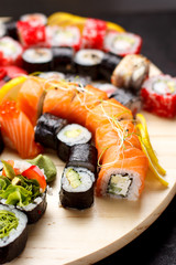 Japanese cuisine. Sushi set on a round wooden board over black concrete background.
