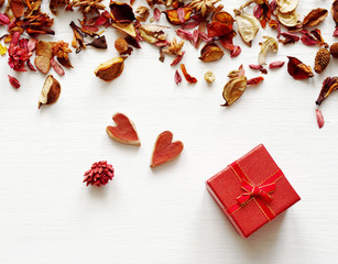 Gift red box with a bow and two red hearts in an environment of dry fragrant flowers on a white wooden background. Greeting card for lovers, friendship or valentine's day.