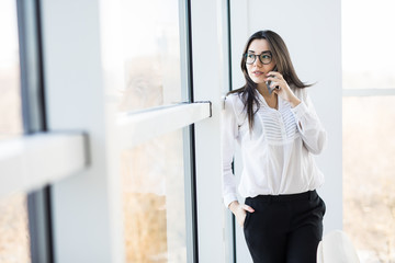 Fototapeta premium Business woman speak on phone near big office windows in modern smart space.