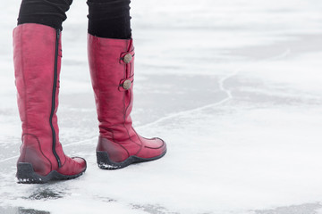 Woman walking on the lake ice surface in winter day.  Red winter boots on legs. Active lifestyle at nature.