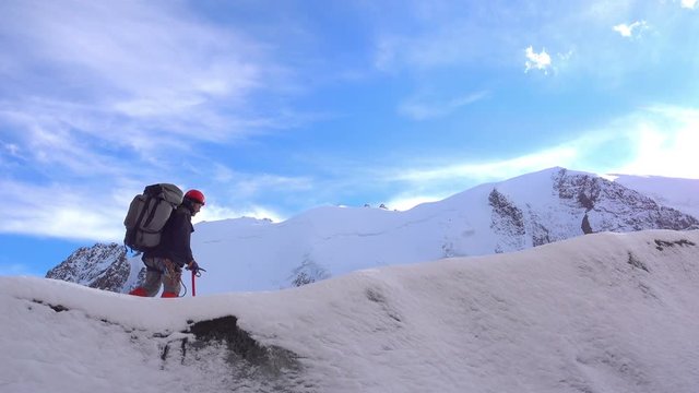 Climber with large backpack using an ice ax goes on a snowy ridge