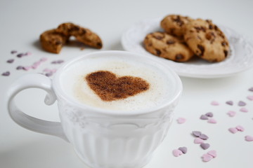 Cappuccino with heart pattern of cinnamon and cookies on the white table