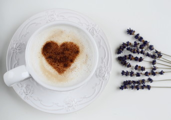 Cappuccino with heart pattern of cinnamon and flowers composition on the white table
