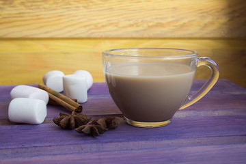 coffee with cream, marshmallows, anise and cinnamon sticks on purple wooden table.