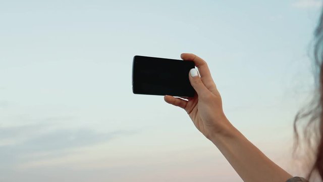 Female hand holding a mobile phone against the sky on the beach, view of the calm sea