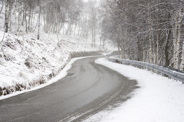 Mountain road in winter with snow and fog, slippery asphalt, difficult driving conditions.