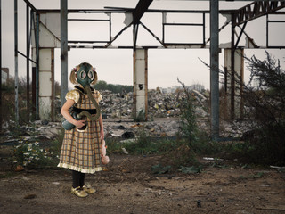 Little girl in a gas mask amidst the ruins. A child in a dress with a broken doll in his hands