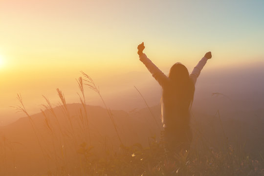 silhouette woman rising hands on mountain in morning