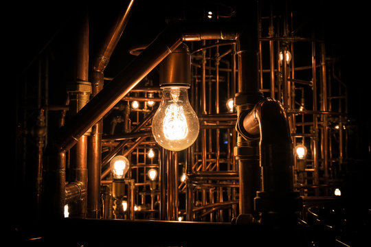 Light in darkness - Incandescent light bulb between rusty pipes