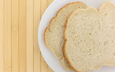 Top close view of English muffin toasting bread slices on a white plate atop a wood place mat.