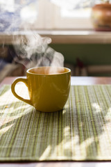 Steam of morning tea above yellow cup on table