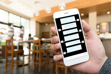 Chat bot and future marketing concept . Hand holding mobile phone with chatbot application in coffee shop