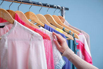 female hand selects colorful clothes on wood hangers on rack in 